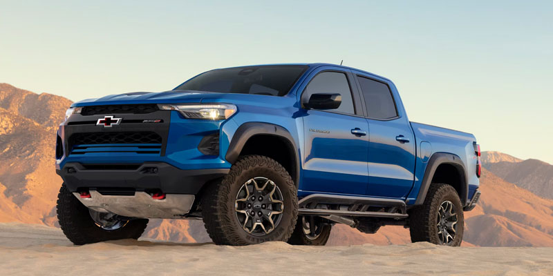 Blue Chevrolet pickup truck driving on desert terrain.