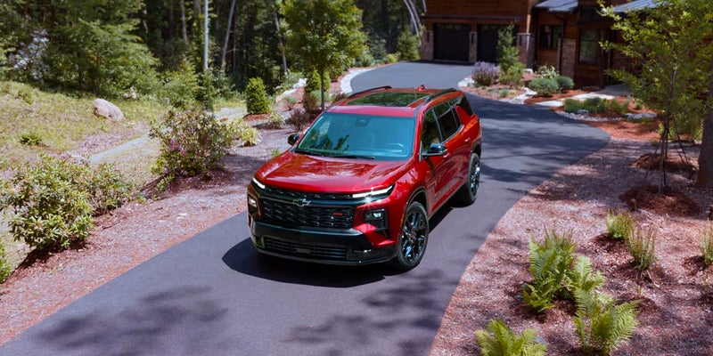 A shiny red SUV with black trim parked on a winding asphalt driveway in front of a rustic house surrounded by trees.